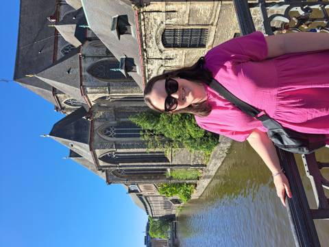 Traveller in pink dress smiling on a bridge beside the medieval church towers and canal of Ghent on a bright sunny day.