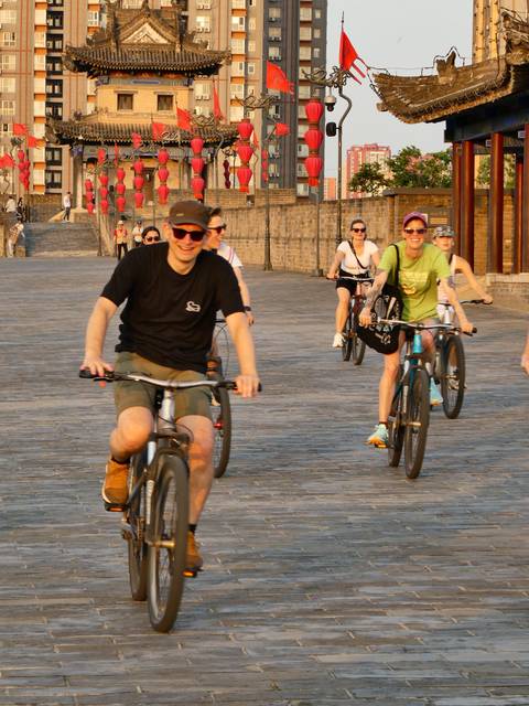 Group of cyclists ride along ancient city walls in warm evening light.