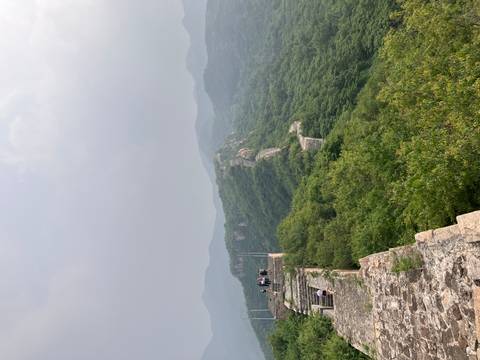 Stone ramparts of the Great Wall snake over green mountains beneath a hazy sky.