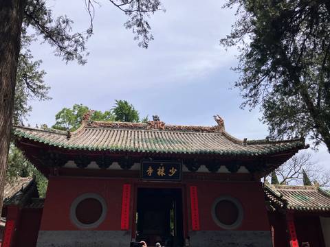 Entrance gate of Shaolin Temple adorned with ornate roof carvings and a black sign under clear skies.