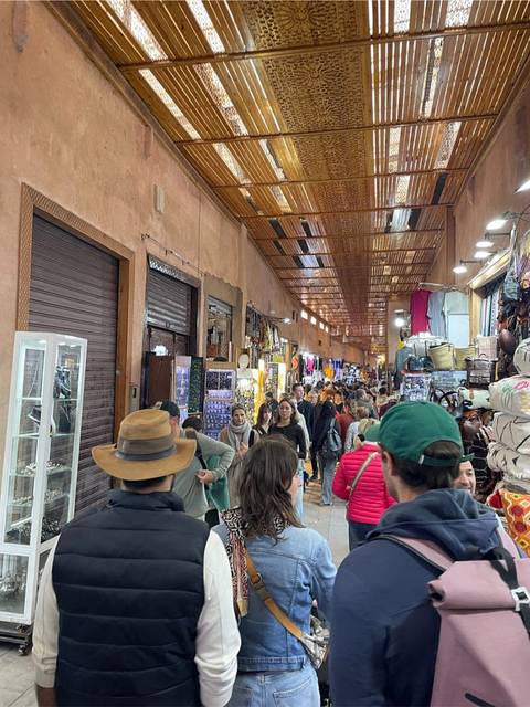 Busy covered market aisle packed with shoppers, souvenir stalls and hanging leather goods in Marrakesh souk.