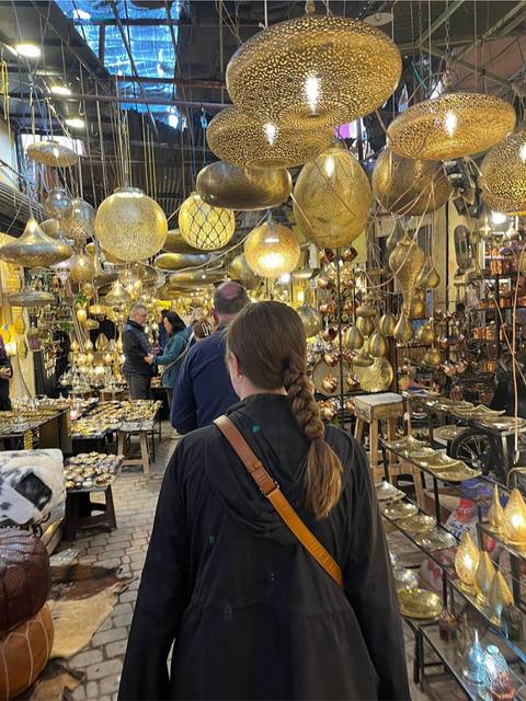 Crowded brass lantern shop glowing with warm lights as a guided group explores the narrow aisle.