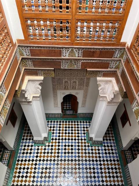 Looking down into a riad courtyard with patterned tiles, carved plaster and a small doorway at the far end.
