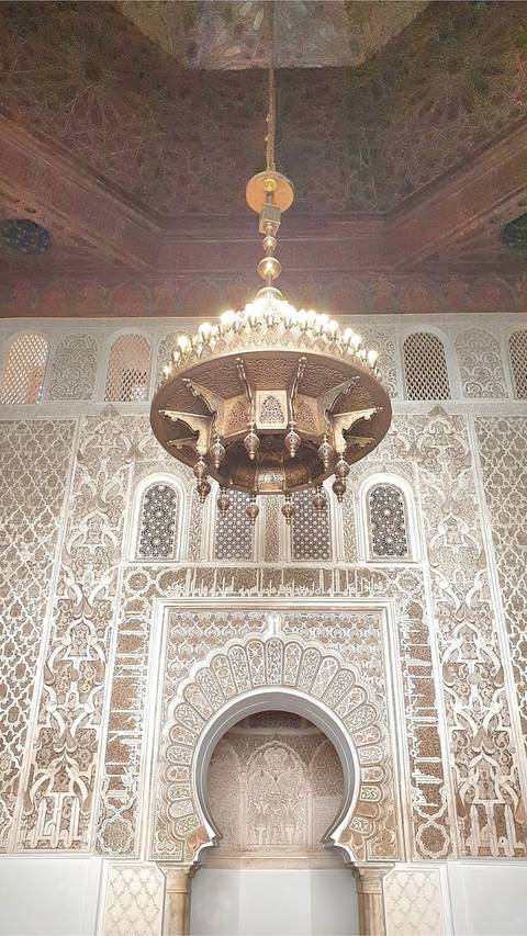 Intricate chandelier hanging in richly decorated interior of a Moroccan madrasa