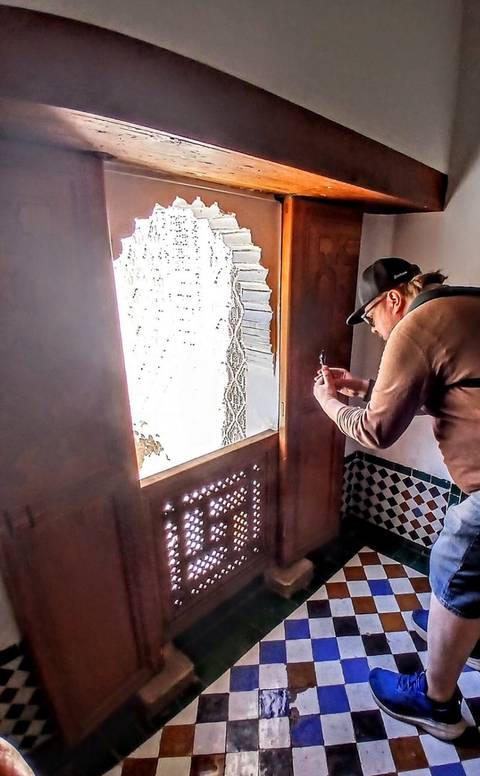 Traveler photographing intricate window lattice inside Moroccan monument