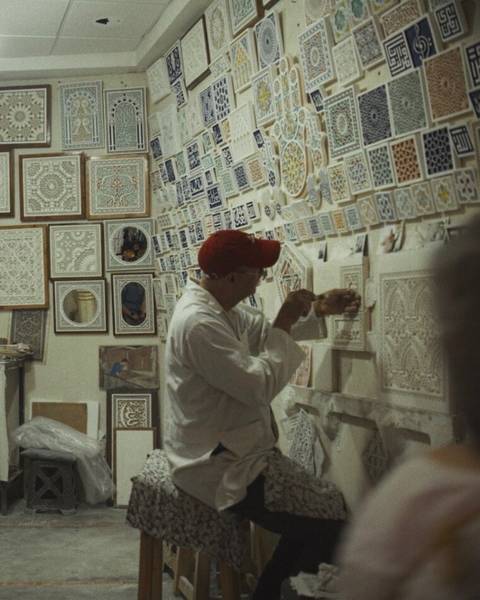 Artisan in workshop carving plaster surrounded by pattern samples