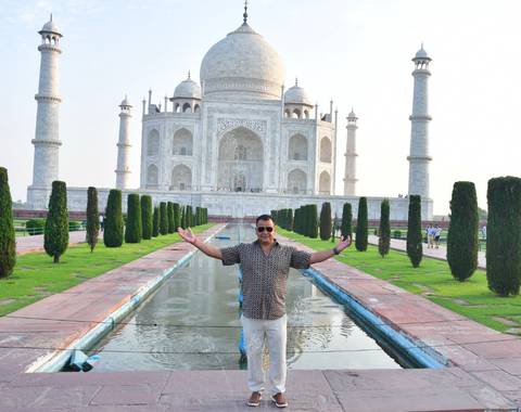 Traveller poses with outstretched arms along the reflecting pool in front of the Taj Mahal.