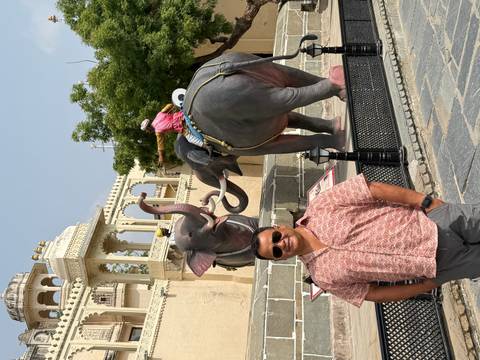 Man smiles before lifelike elephant statues outside ornate palace gateway in Udaipur.