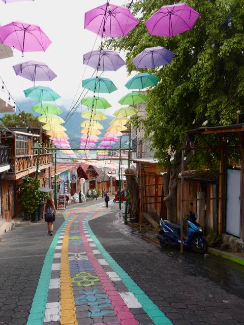Colorful umbrellas hang over a lively pedestrian street in San Juan La Laguna.