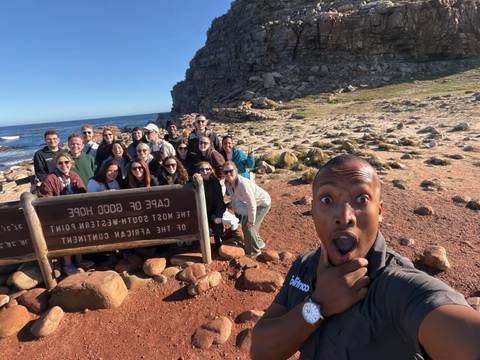 Duplicate angle of tour group selfie at Cape of Good Hope with dramatic rocky coast behind.