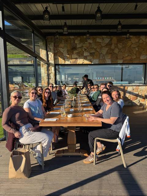 Tour group enjoys a long outdoor dining table with scenic glazing overlooking vineyards.