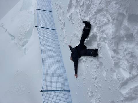Person lies spread-eagled making a snow angel on a high-altitude snowy slope.
