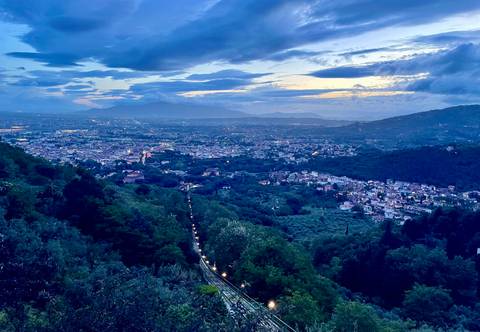 Elevated panoramic view over an Italian city valley with evening lights under dramatic clouds and blue sunset tones