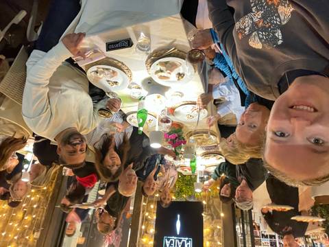Large group of travelers enjoying dinner together at an outdoor restaurant table filled with food and drinks