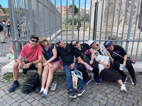 Tired travelers sitting on a stone bench beside an iron fence in a busy historic city square