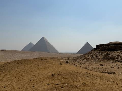 Distant view of the three Pyramids of Giza rising above sandy desert terrain in hazy light