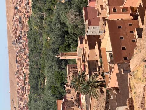 View over adobe village and minaret with lush oasis and arid hills beyond.