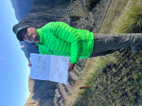 Guide in bright green jacket holds up a route map while standing above the terraces of Machu Picchu at sunrise.
