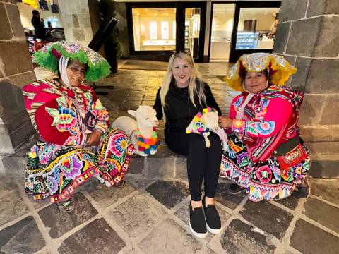 Tourist sitting with two Peruvian women in vibrant traditional attire holding decorated baby alpacas