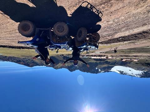 Two travellers on blue quad bikes celebrating in rugged Andean highlands with snow-capped peaks behind