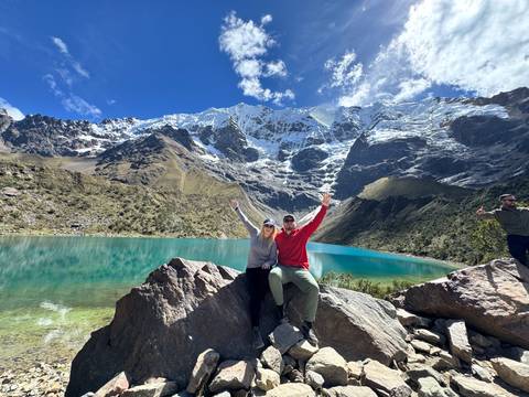Couple posing on rock beside turquoise alpine lake with glacier-covered Andes towering behind