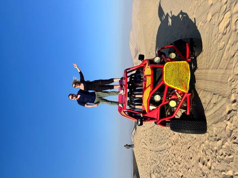 Couple standing on roof of red dune buggy celebrating in open desert under blue sky