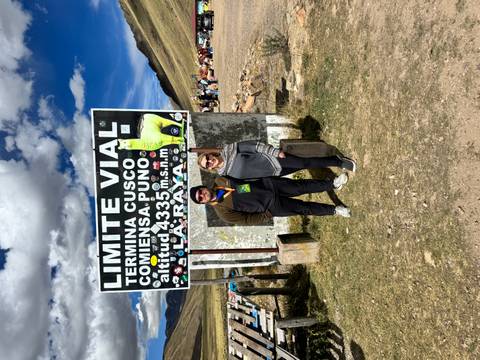 Couple smiling beside roadside sign marking the high-altitude pass between Cusco and Puno