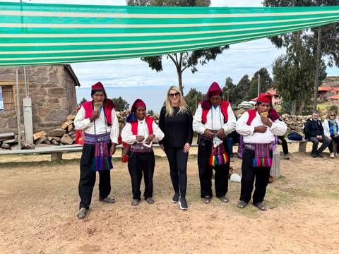 Traveller posing with traditionally dressed islanders under a sunshade with Lake Titicaca in background
