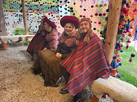 Visitors seated in colourful ponchos inside a craft workshop decorated with pom-poms