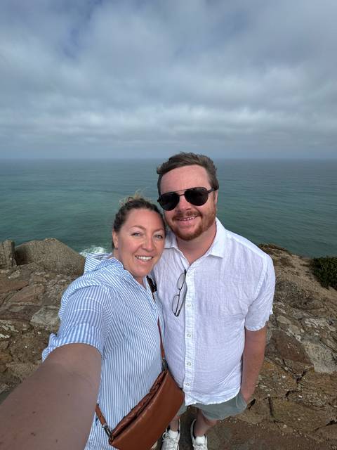 Couple selfie atop rugged Atlantic cliff with vast ocean backdrop under hazy sky