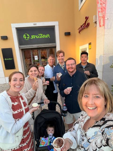 Smiling group selfie enjoying ice cream in front of a small shop on a cobblestone street