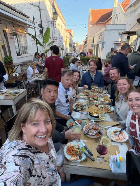 Friends gathered around an outdoor table covered with Portuguese seafood dishes and drinks