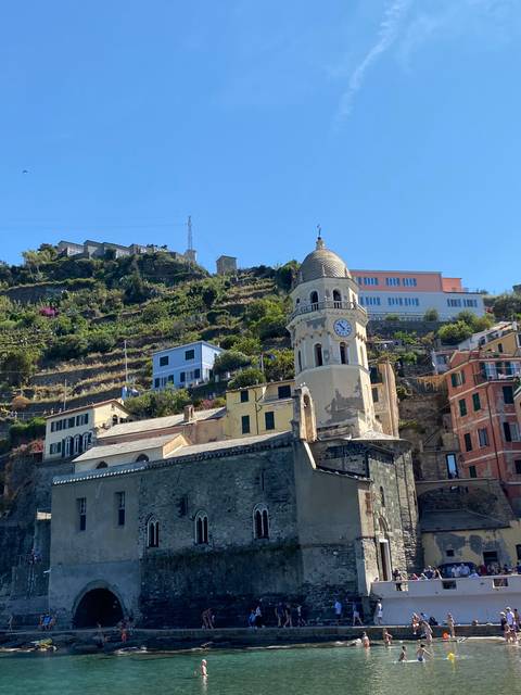 Clock-tower church stands against terraced hillside vineyards in bright morning sun.