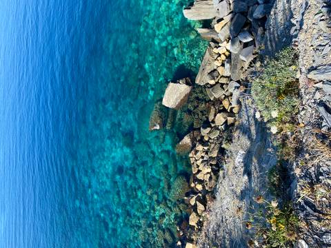 Crystal-clear turquoise sea laps against rocky shoreline viewed from above.