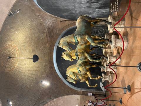 Four gilded bronze horses of St. Mark’s Basilica displayed under a brick vault with spot lighting.