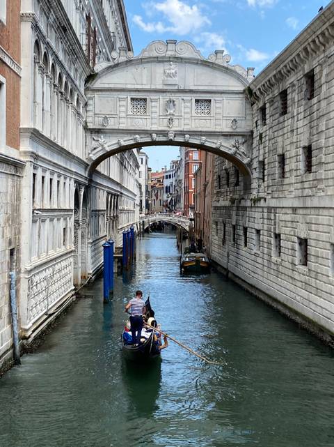 Gondolier steers under the ornate white Bridge of Sighs spanning a narrow Venetian canal.