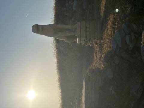 Ancient stone lion statue stands on a pedestal against a sunlit grassy hill at dawn.