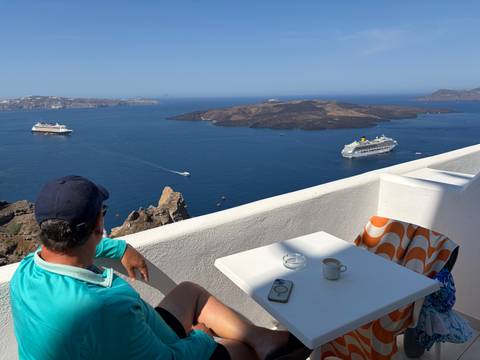 Man relaxes at a white terrace overlooking Santorini caldera with cruise ships below.