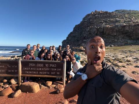 Selfie of enthusiastic tour group at Cape of Good Hope sign with rocky coast behind.