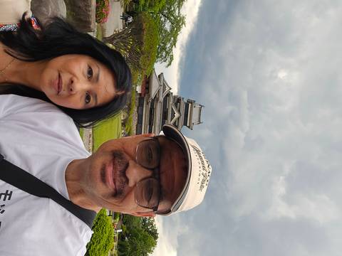 Selfie of couple with Matsumoto Castle behind them under looming grey clouds.