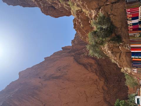 Steep red-rock walls of Todra Gorge rising toward a bright midday sun with colourful market stalls below
