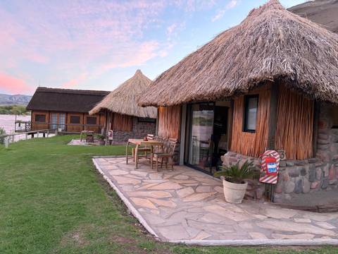 Thatched-roof riverside chalets with stone patios and lawn at dusk