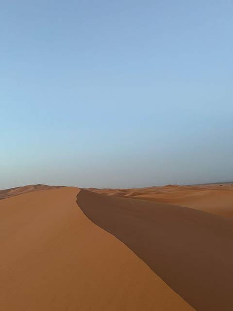 Minimalist view of a curving sand ridge against a pale blue sky in the desert