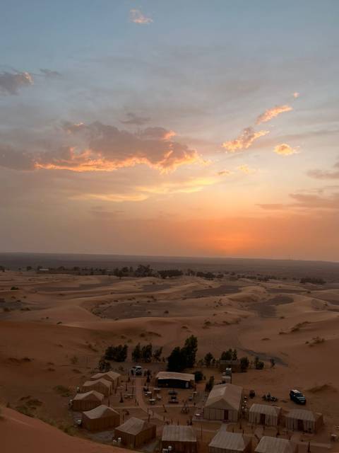 Orange sun dips below the horizon casting warm light over desert plains and scattered palms