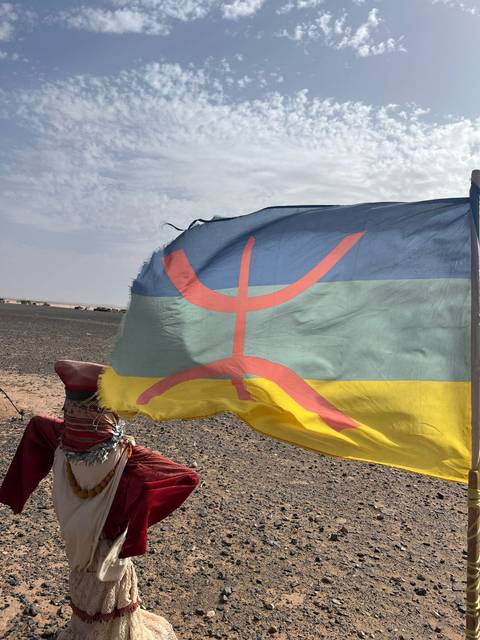 Amazigh (Berber) flag ripples in the desert wind with black gravel plain behind