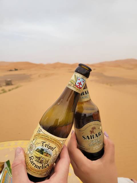 Two chilled beer bottles clink together with golden dunes softly blurred in the background