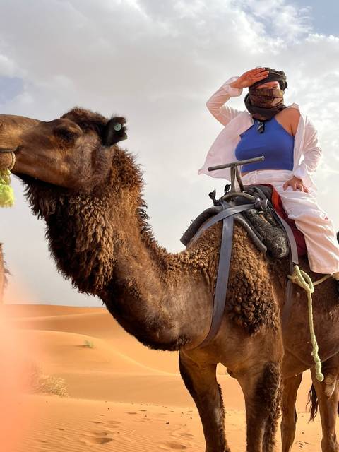 Close-up of shaggy camel with a rider in flowing white trousers and blue top