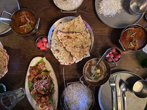 Top-down view of a wooden table filled with assorted Indian dishes, breads, rice and pickles.