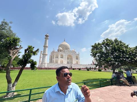 Tour guide speaking with the Taj Mahal and manicured gardens in the background on a bright day.
