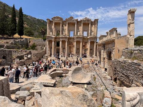 Crowds explore the ornate façade of the ancient Library of Celsus amid scattered marble ruins.